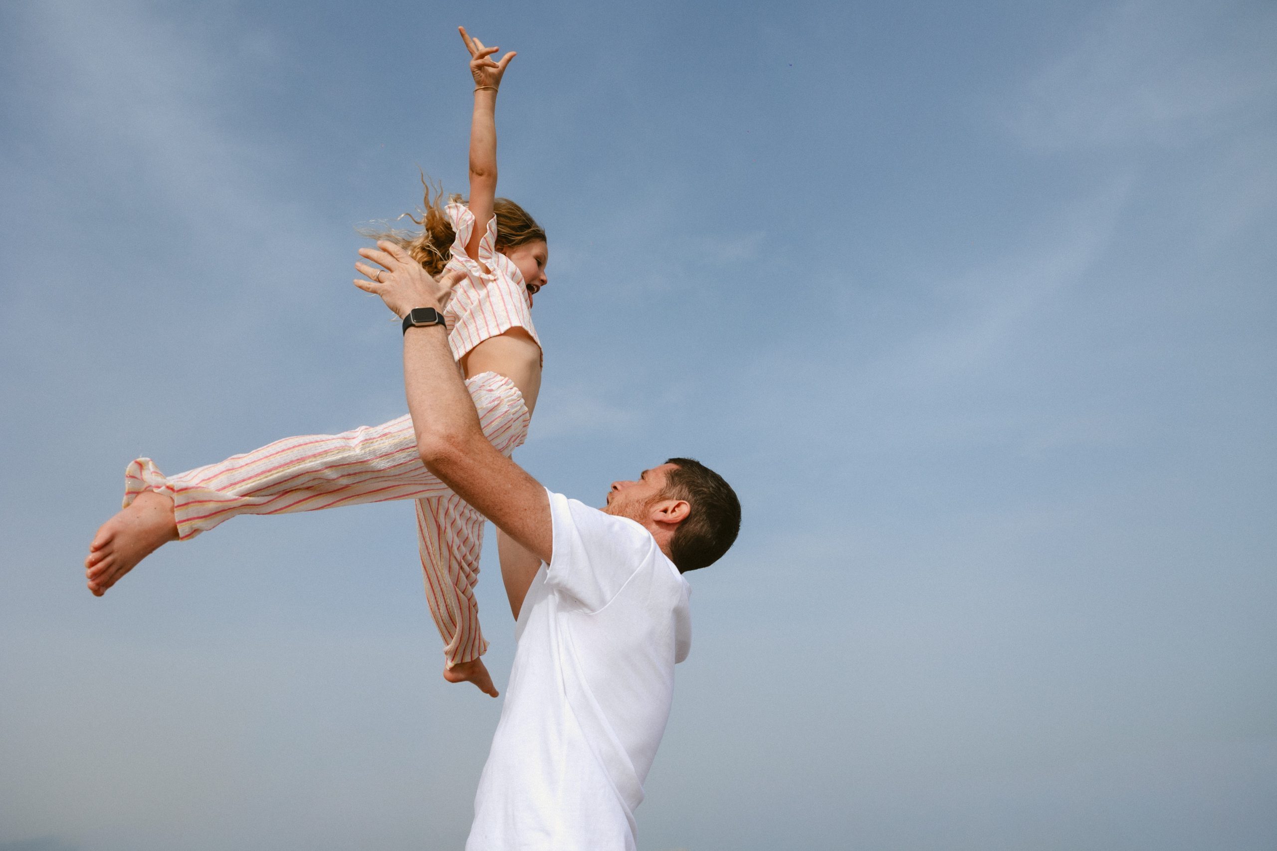 Petite fille jouant avec son papa qui la soulève dans le ciel